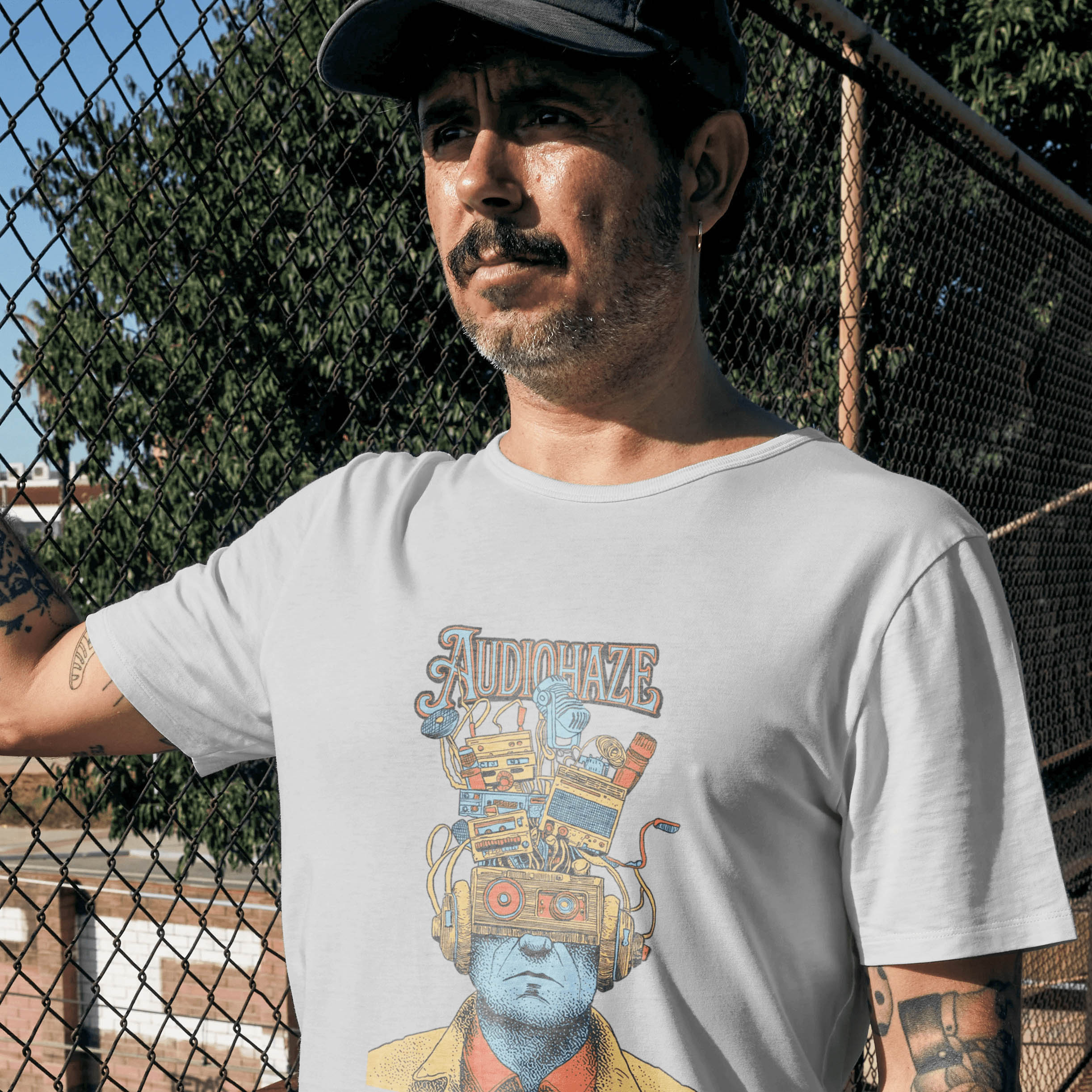 Portrait of a model wearing a white Audiohaze graphic T-shirt near a chain-link fence
